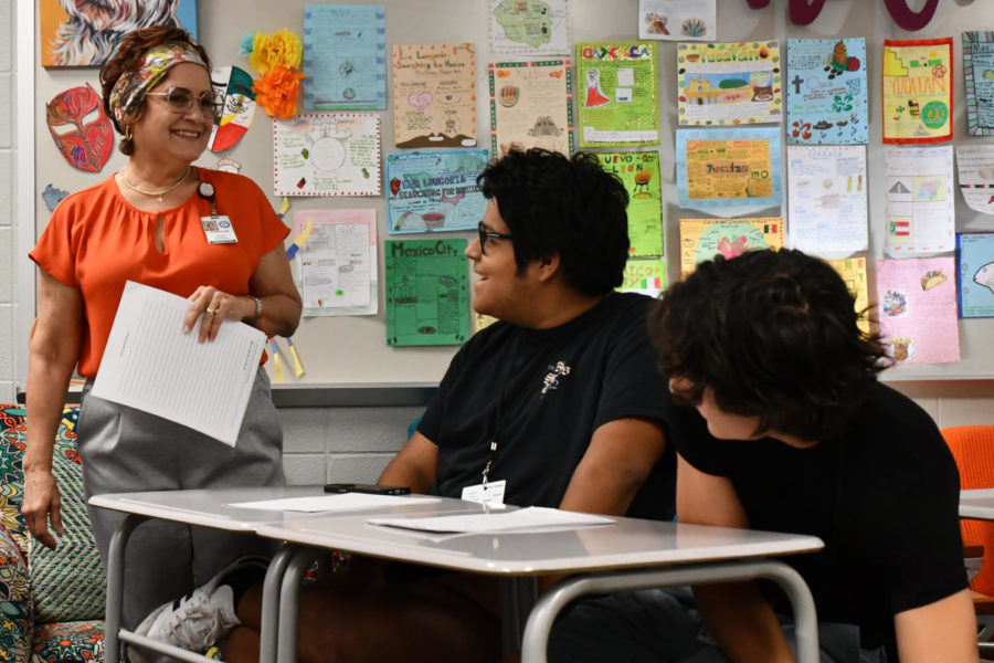 While passing out papers, AP Spanish 5 teacher Eileen Quiñones talks to juniors Andrick Lopez and Luke Cavallo. 