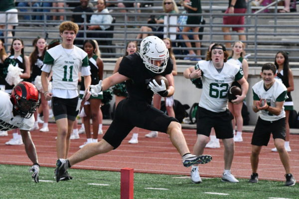 Senior Aiden Troost jumps into the endzone for the first touchdown of the game against Porter while JV football players cheer him on from the sidelines.