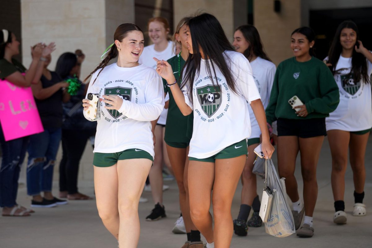 Seniors Reese Shaw and Sienna Morales laugh together as they walk through a tunnel of parents, friends and siblings cheering them on before they got on the charter bus to head to the Area playoff game.