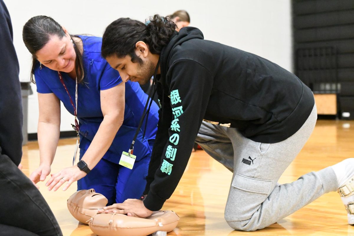 School nurse Mary Fischer shows Zain Qamar, 12, where to place his hands to give CPR. The senior class attended
a mandatory meeting to discuss senior week and meet their CPR
training graduation requirement.