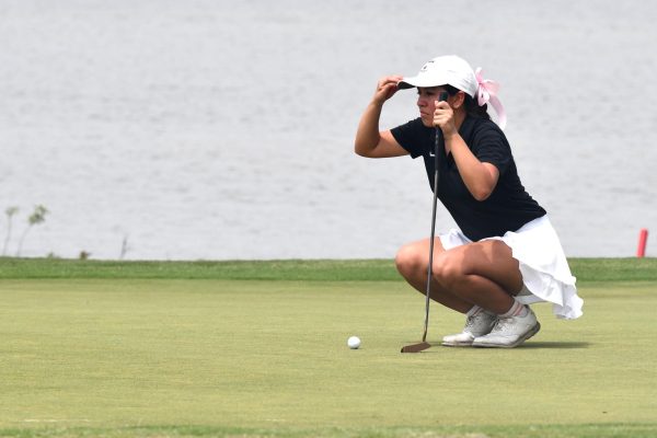 Senior Leah Torres grabs her ball-marker from her hat while she lines up her putt.