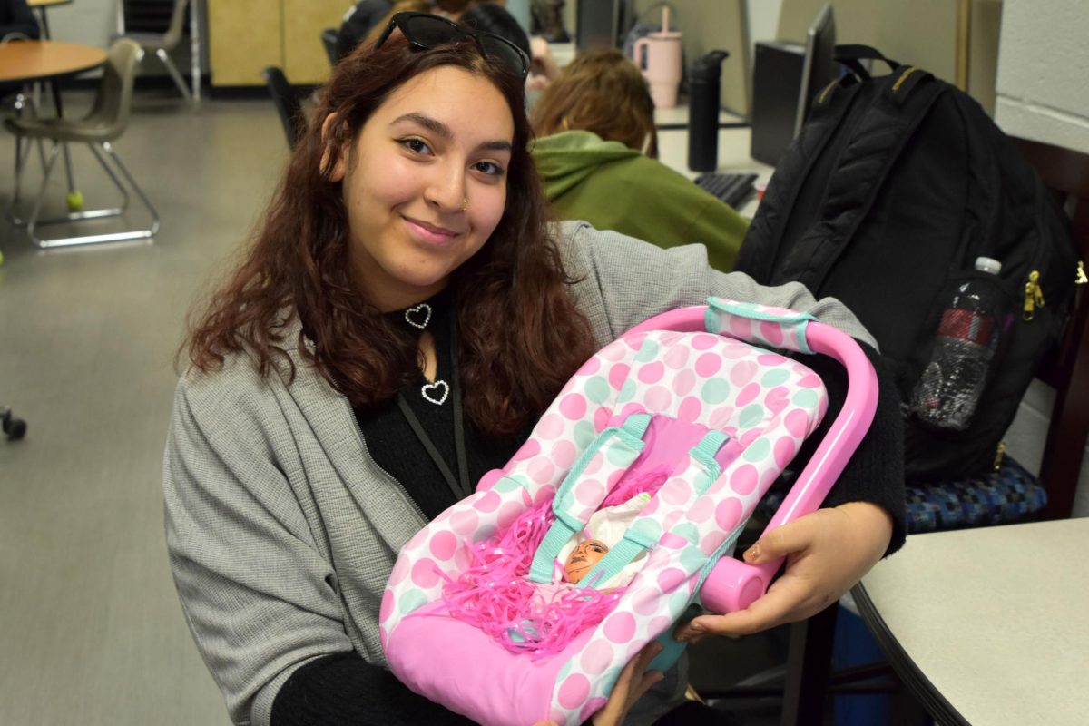 Junior Beste Kaya holds her egg baby in a carrier for the project in her child development class.