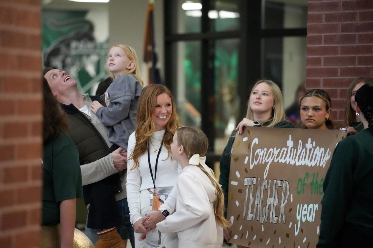 Prior to the celebration parade, science teacher Cassandra Debottis smiles to students as her husband and daughters look at all the students gathering for the march through the halls.