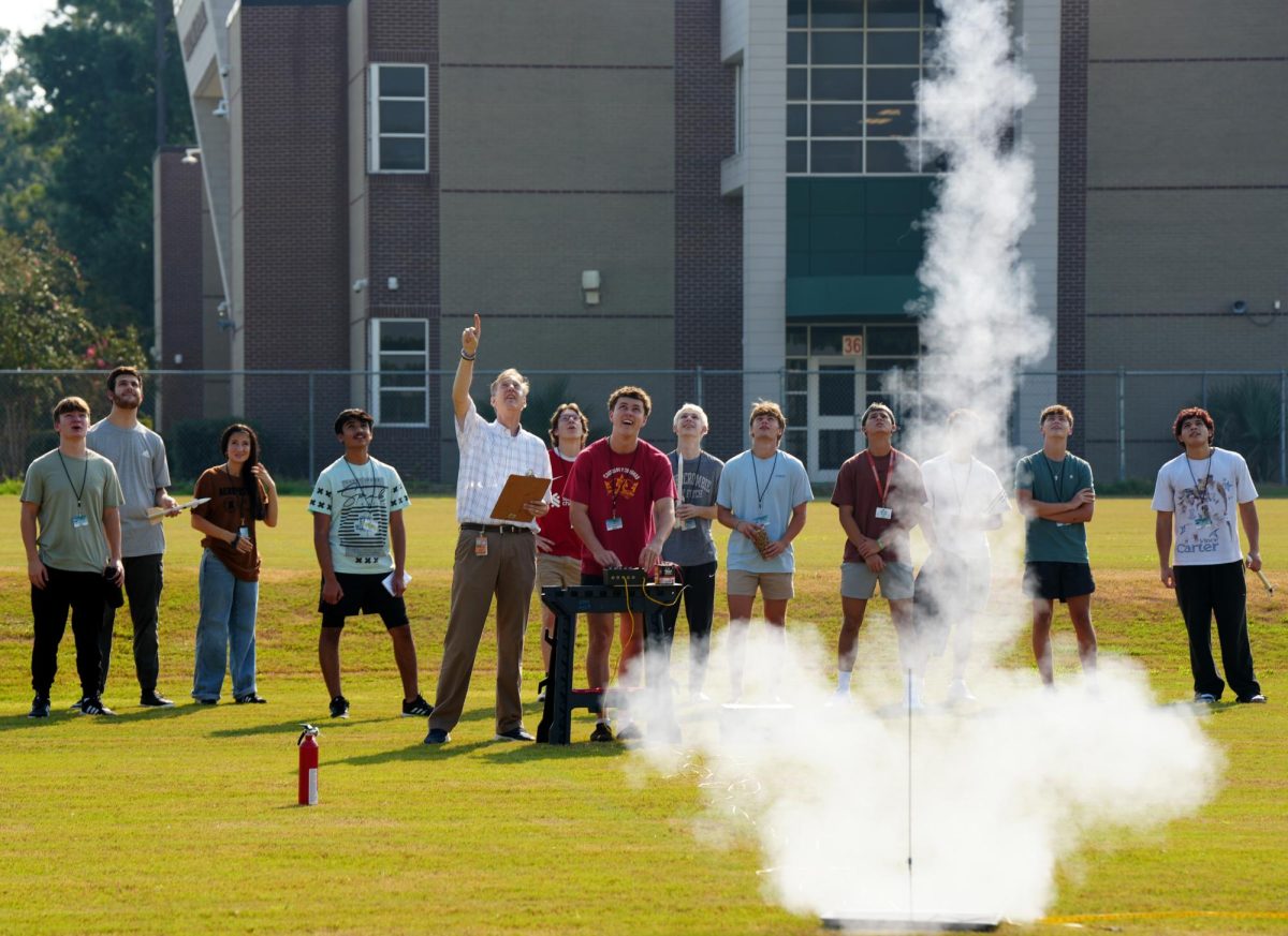Glenn Taylor aeroscience class watches as senior Ronan Flaherty launches his rocket on the practice field near the school.
