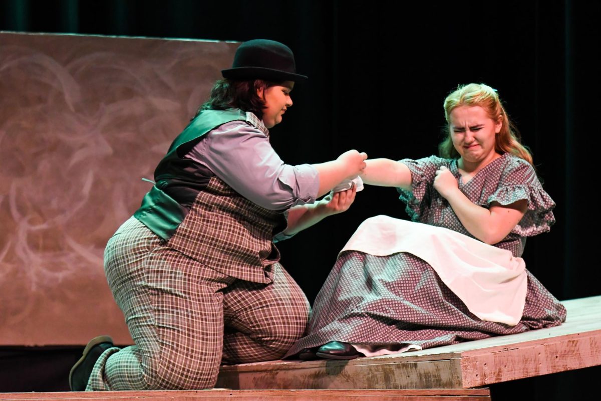 Galen P. Gray, played by junior Ada Stokes, applies a salve onto the arm of Tiny Wingfield, played by senior Emerson Harris. 