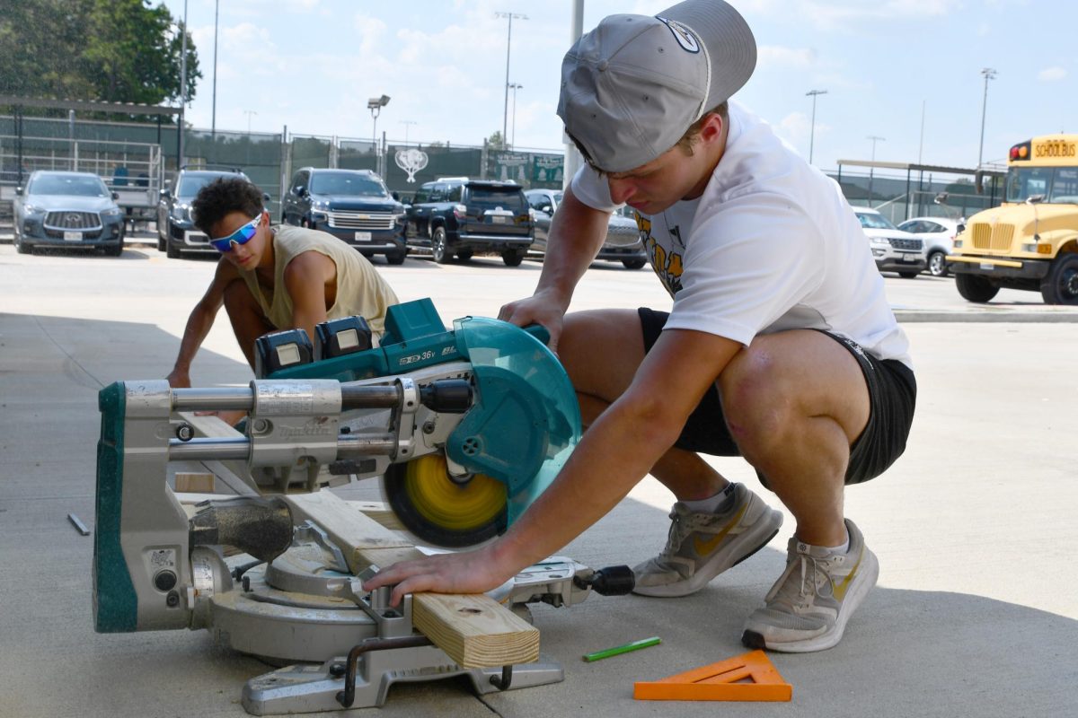 Seniors Joaquin White and Cooper Wolocko cut a piece of wood on the power saw for the walls of the latest Tiny Home.