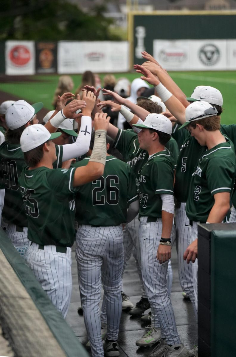 While senior Landon Coburn walks into the dugout after scoring a run, his teammates celebrate with Coburn. 
